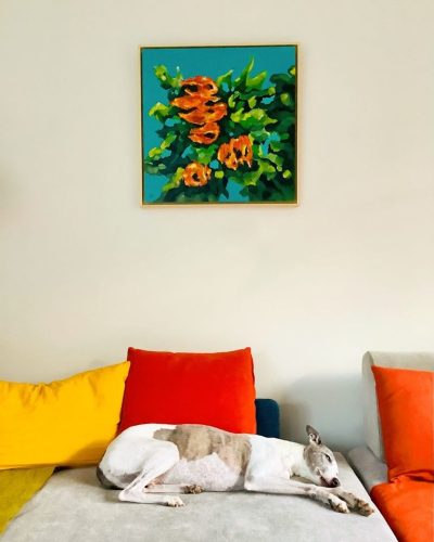 Dog on sofa under painting of red flowers